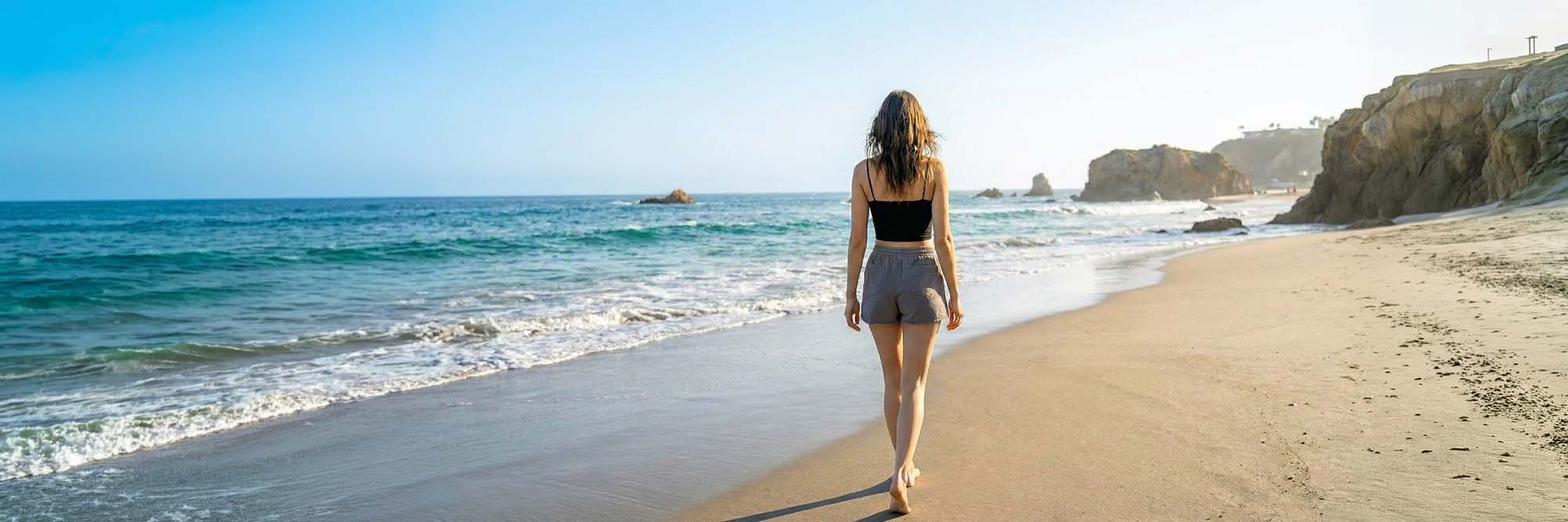 A woman walking on the beach in California wearing an organic crop top and shorts.