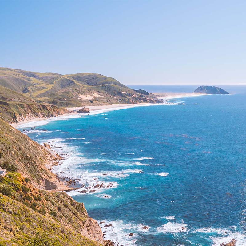 Big Sur California Coastal landscape with blue ocean, green hills, and clear sky