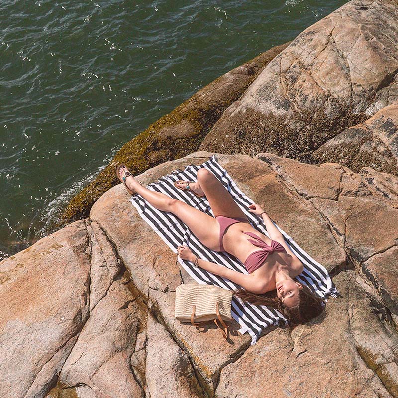 A woman laying on rock beside the ocean wearing an organic sustainable bikini in dusty rose color