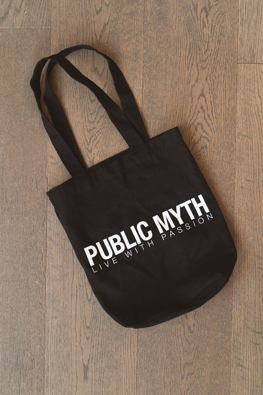 Black cotton canvas tote bag with 'Public Myth' text on a wooden surface