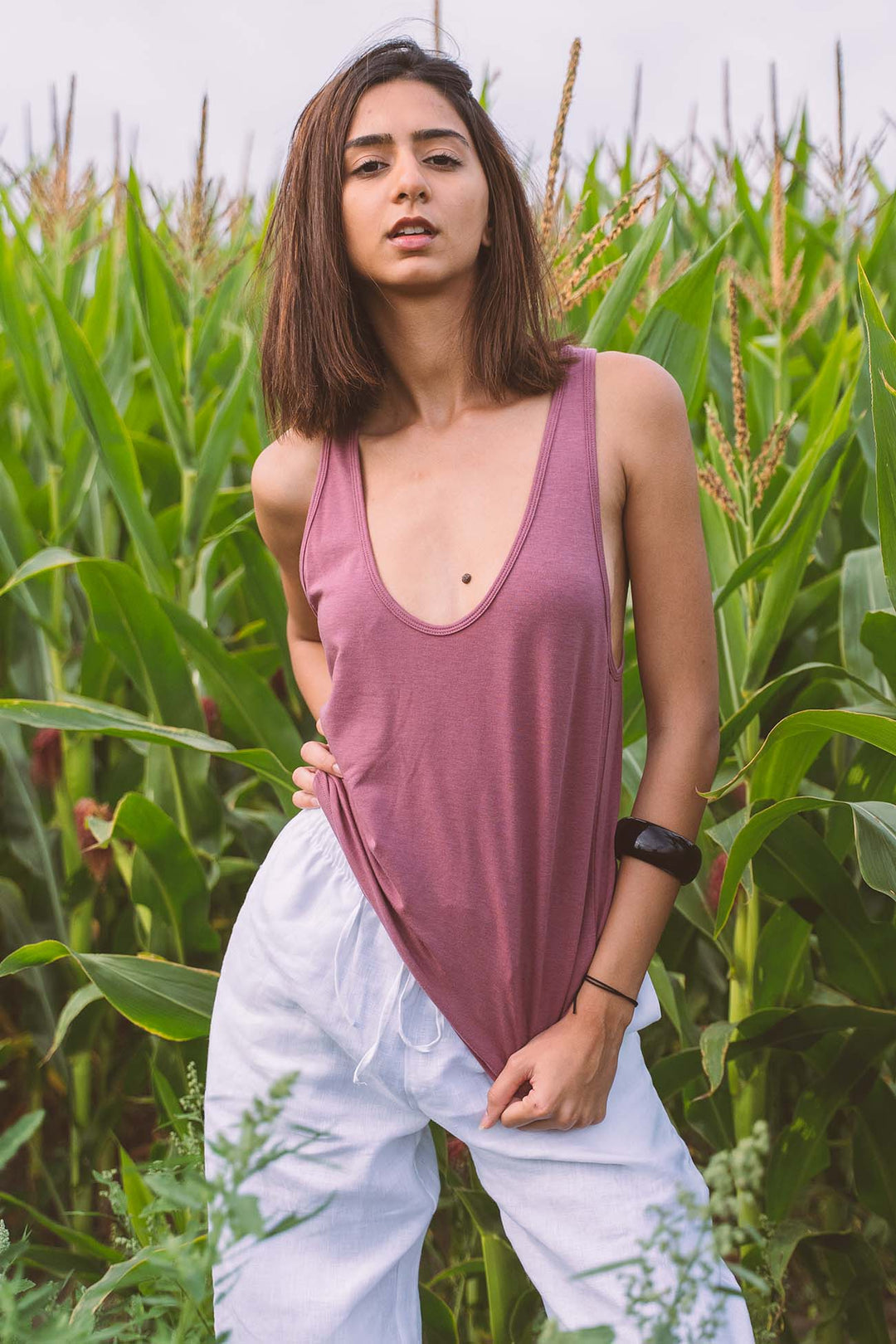 A woman wearing the Aria Dusty Rose Organic scoop neck tank top with low cut armholes with white linen pant